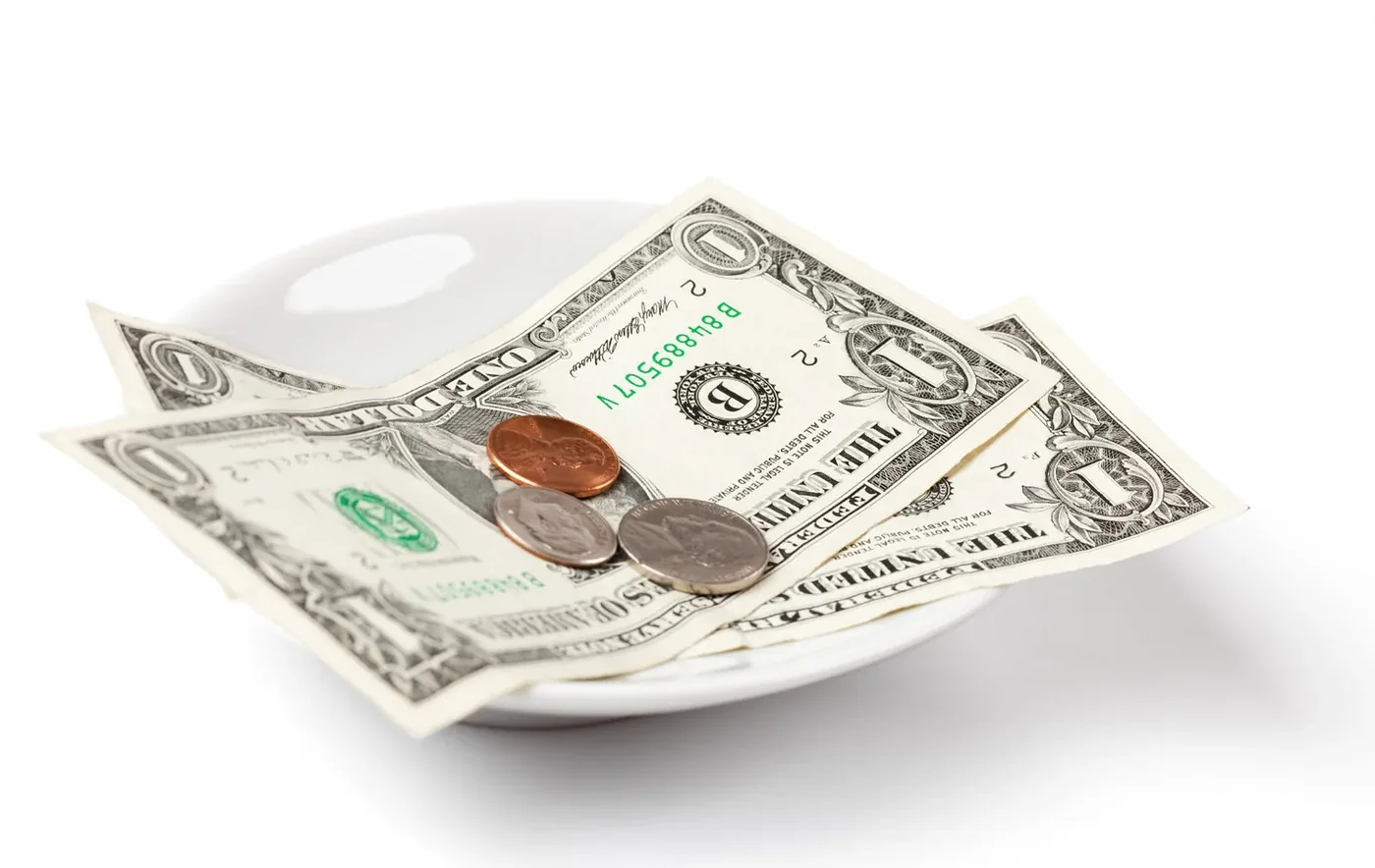 Banknotes and coins left as a tip on a white plate