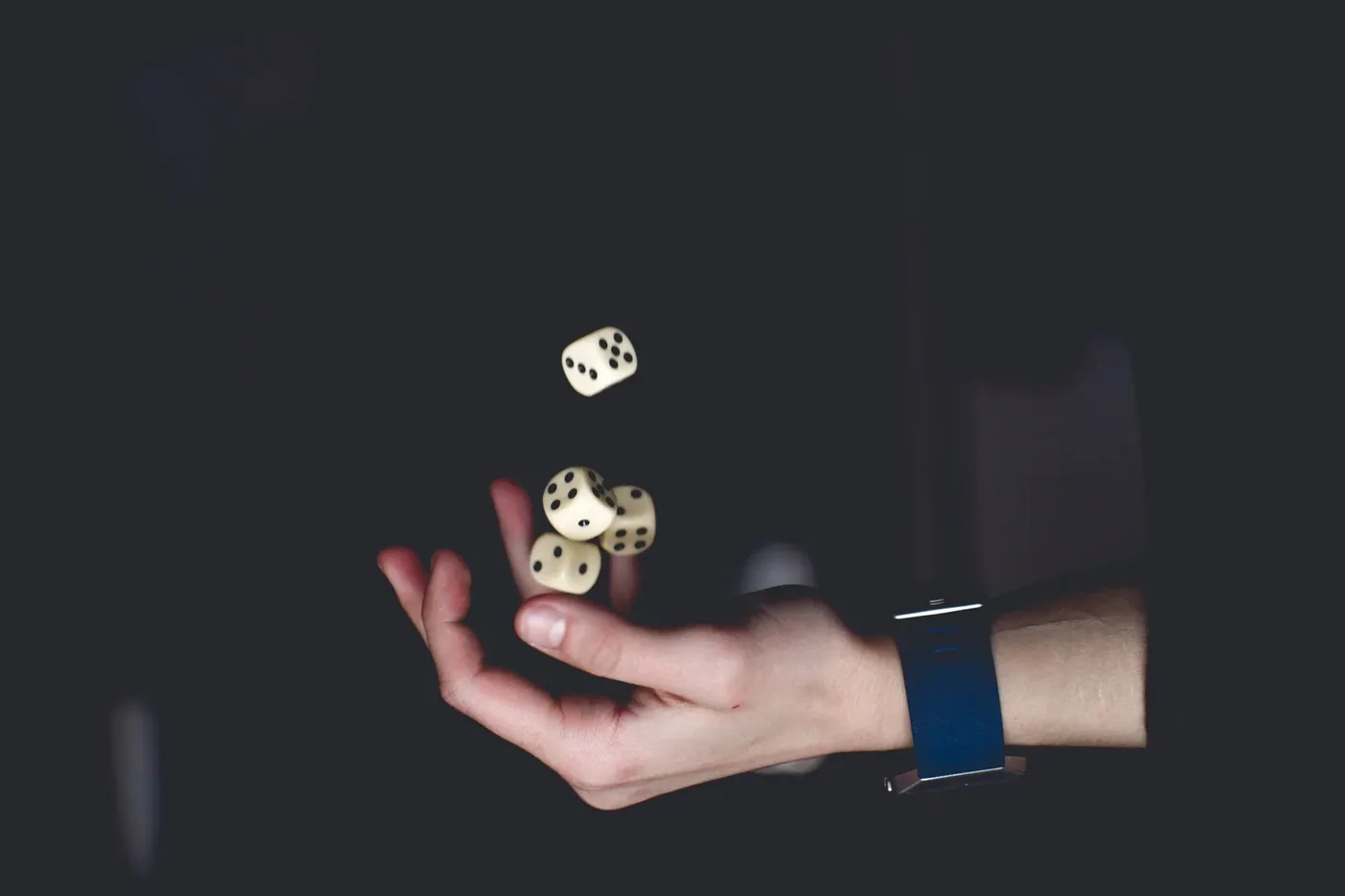 Hand tossing three dice against a dark background